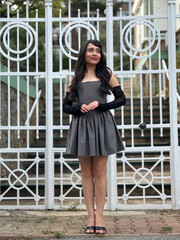 Beautiful brunette girl posing in sexy and fashionable clothes in front of white old-style iron gate. Full length shot outdoors in daylight