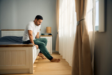 Depressed man in pajama sitting on edge of his bed at home. Copy space.