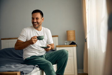 Happy man having cup of coffee in bedroom in morning.