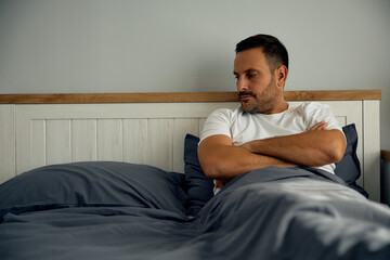 Sad man missing someone while looking at empty place on his bed. Copy space.