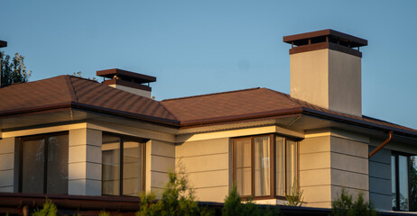 A contemporary home features a striking sloping roof and stylish architecture, illuminated by the warm hues of a setting sun, nestled among lush greenery and landscaping