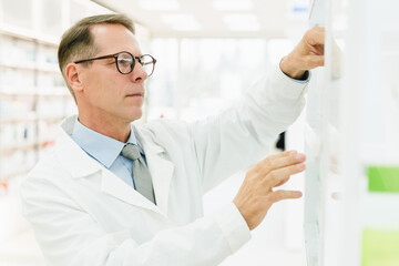 Male middle-aged caucasian pharmacist druggist looking searching for the remedy pill on the shelves at drugstore pharmacy