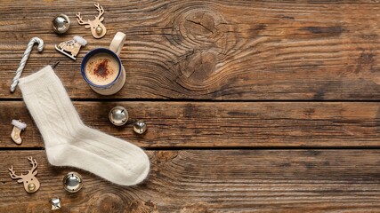 Knitted socks, Christmas decorations and cup of coffee on wooden background with space for text