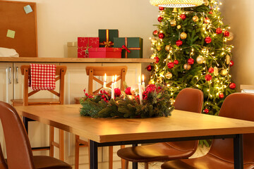 Christmas composition with wreath, burning candles, red berries and balls on table in kitchen at evening