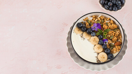 A healthy nutritious breakfast of natural Greek yoghurts, granola and fresh berries on pink background. Copy space