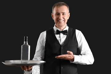 Mature waiter with bottle of vodka on black background