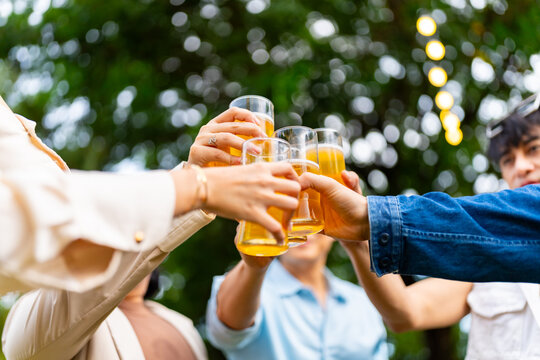 Group of Happy Asian millennial generation people friends enjoy and fun toasting beer glasses celebration reunion meeting at outdoor dinner party in the garden at restaurant on holiday vacation.