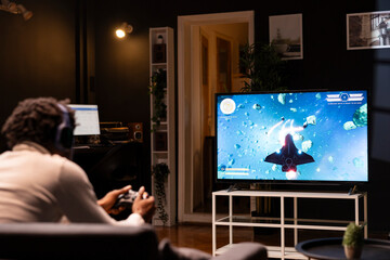 Gamer using controller and headphones to immerse himself in classic arcade videogame on smart TV,...