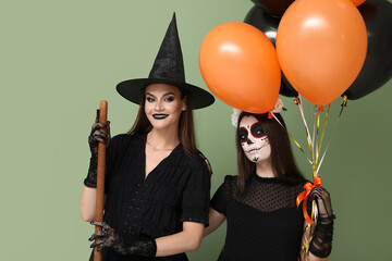 Young women dressed for Halloween with balloons on green background