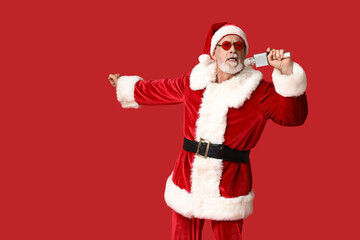 Santa Claus in sunglasses with microphone singing on red background