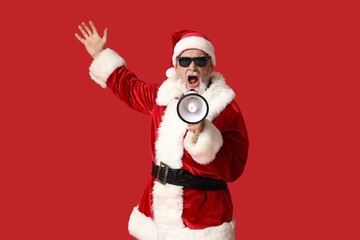 Santa Claus in sunglasses with megaphone screaming on red background