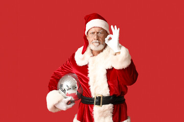 Displeased Santa Claus in glasses with disco ball showing OK gesture on red background