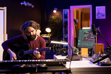 Young music producer playing guitar and creating songs using digital daw software. Musician singer...