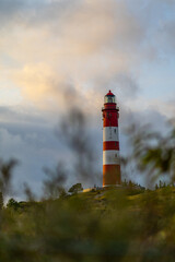 Lighthouse standing tall atop a hill with a colorful striped tower under a cloudy sky at sunset