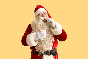 Santa Claus eating cookie with milk on yellow background