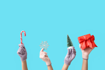 Female hands in warm gloves with Christmas decorations and gift box on color background