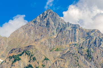 Scenery of high mountain peak over blue sky with white clouds.