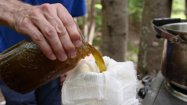 Herbalist pouring liquid from a jar into cheesecloth captures the essence of traditional herbal preparation in slow motion. Selective focus