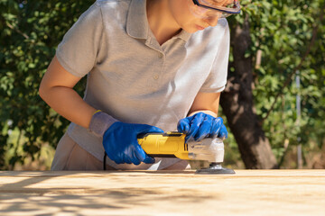 Carpenter Woman Sanding A Wooden Plank Outdoors Using An Electric Sander Outdoors