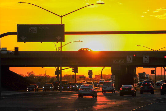 Afternoon traffic is silhouetted by the bright yellow-orange sunset light at Loop 202 and Elliot Road in southeastern Maricopa County, Arizona