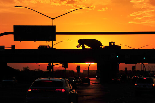 Bright yellow-orange sunset light silhouettes the vehicular traffic on a hot summer day at the Loop 202 underpass at Elliot Road in Mesa, Arizona