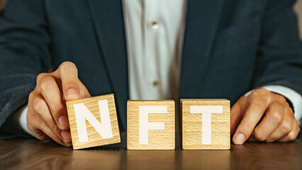 There is wood cube with the word NFT. It is an abbreviation for Non-Fungible Token as eye-catching image.