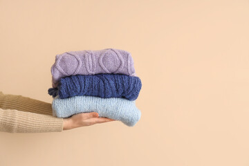 Woman with folded sweaters on beige background