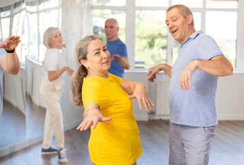 Obraz premium Group of elderly women and men in sportswear learn to dance the foxtrot in a choreographic studio