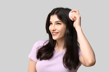 Beautiful young woman brushing her hair on grey background