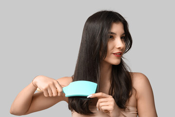 Pretty young woman brushing her hair on grey background