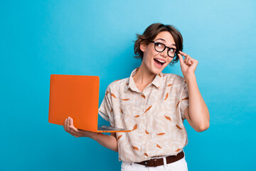 Photo of astonished smart person hold netbook arm touch eyewear look empty space isolated on blue...
