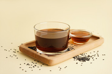 Wooden tray with glass bowls of oil and sesame seeds on beige background