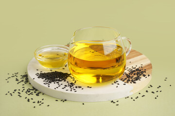 Glass jug and bowl of oil with sesame seeds on green background
