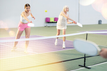 Portrait of expressive young sportswoman playing doubles pickleball with experienced female partner...