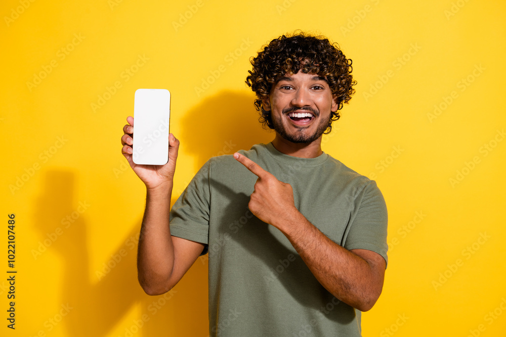 Sticker Photo of positive guy dressed t-shirt indicating at menu on smartphone touchscreen empty space isolated on yellow color background