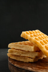 Wooden board with delicious Belgian waffles on black background