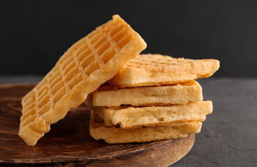 Wooden board with tasty Belgian waffles on black background