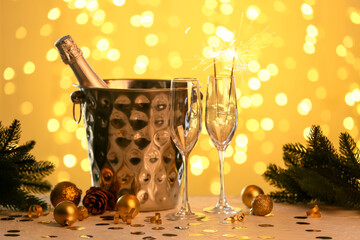 Ice bucket with bottle of champagne, glasses and Christmas decor on table against blurred lights