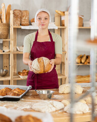 Young female baker in uniform holding basket with homemade bread
