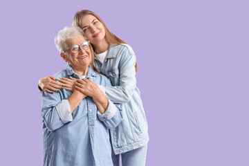 Happy senior woman and her granddaughter hugging on purple background