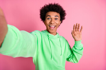 Photo of nice young man take selfie arm wave wear green hoodie isolated on pink color background