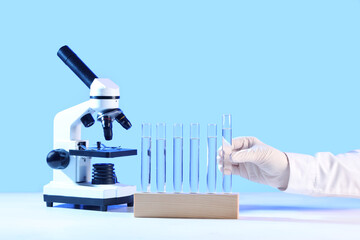 Scientist's hand with test tubes and modern microscope on white table