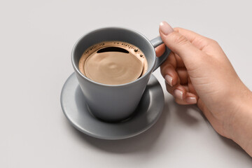 Female hand with cup of coffee on grey background