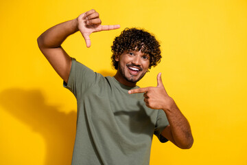 Photo of cheerful guy with wavy hair dressed khaki t-shirt fingers showing frame symbol...