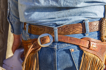 Cowboy wearing leather chaps and blue jeans.