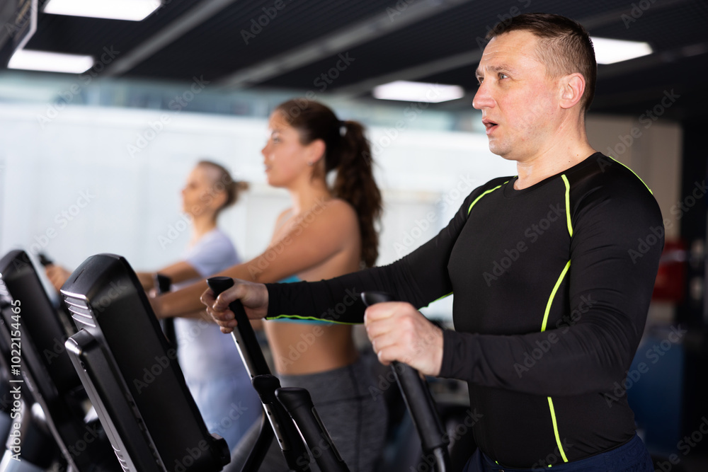 Wall mural strong sportsman training at elliptical machine in gym