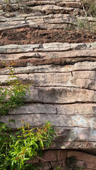  A natural rock formation showing horizontal layers of rock with some greenery growing at the base. rugged, outdoor environment.