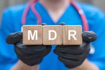 Doctor in black gloves holding wooden cubes sees acronym: MDR. Concept of Medical Device Regulation...