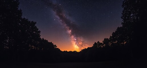 Milky Way galaxy glowing above trees at sunset.