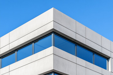 Modern Concrete Building with Minimalist Design, low angle shot, large windows, smooth surfaces, clear blue sky, geometric architecture, bright lighting.